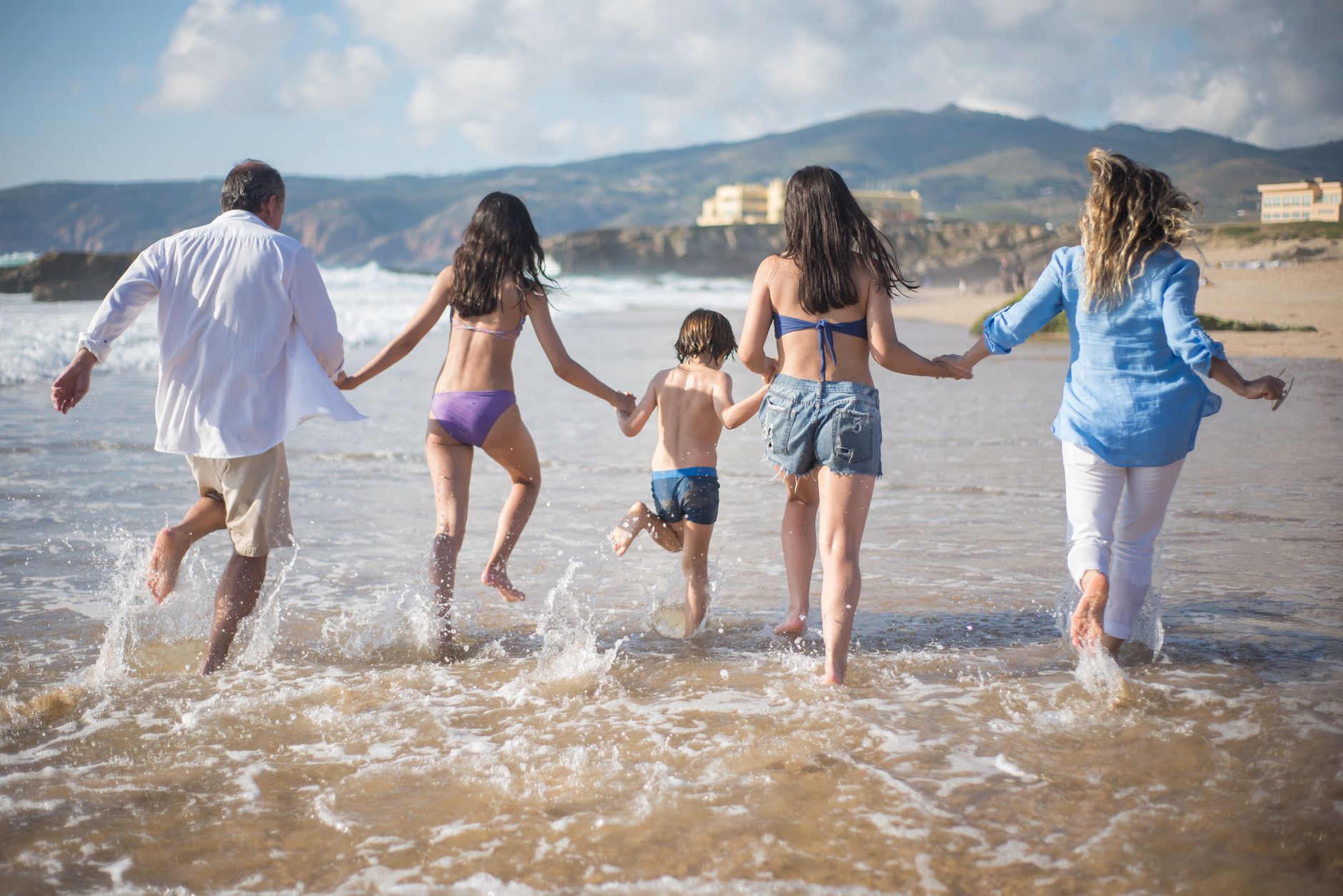 Parents and children walking along a sunny beach with luggage and smiles