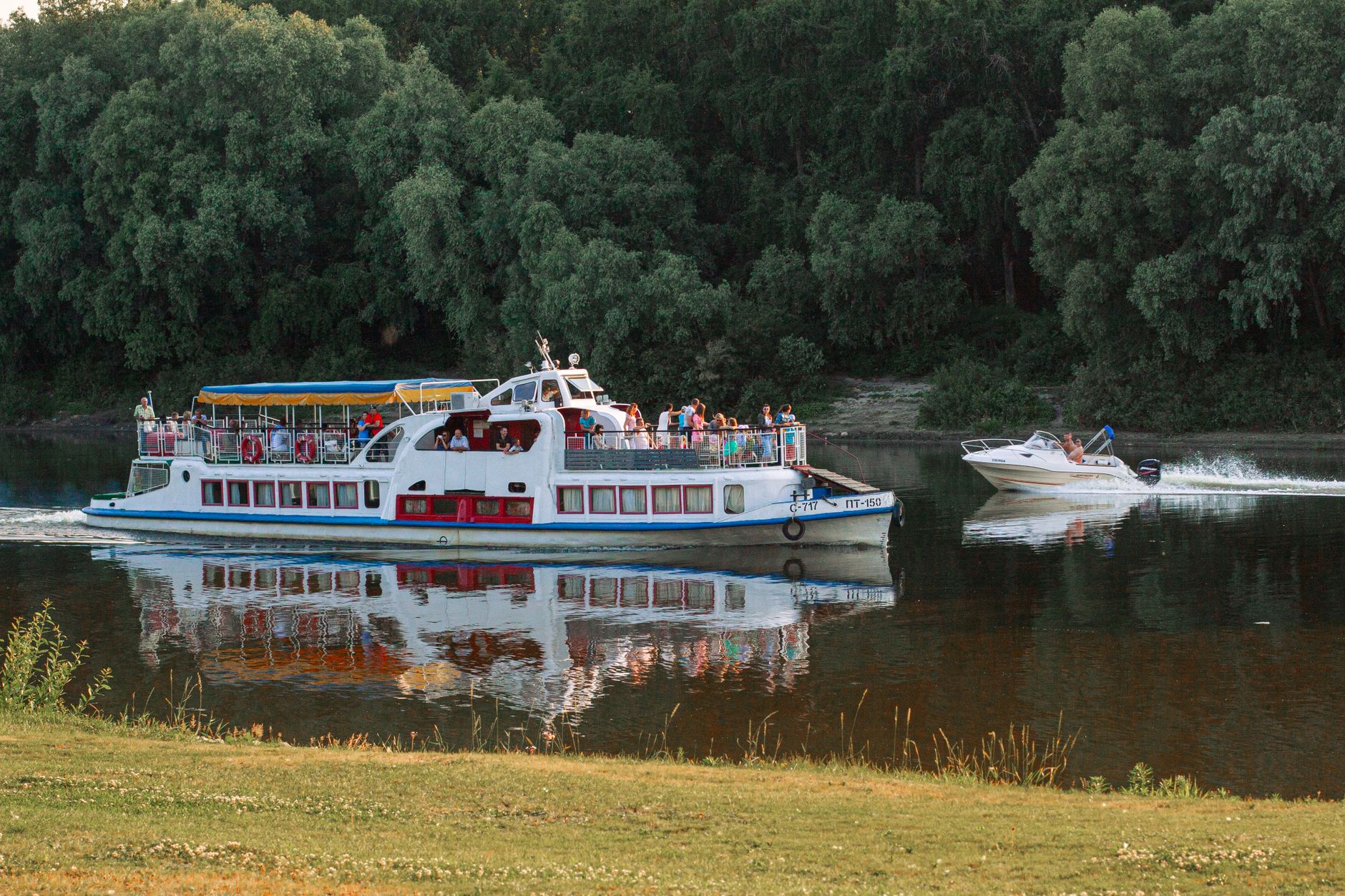 A small river cruise ship gliding through a lush green valley with historic villages along the bank