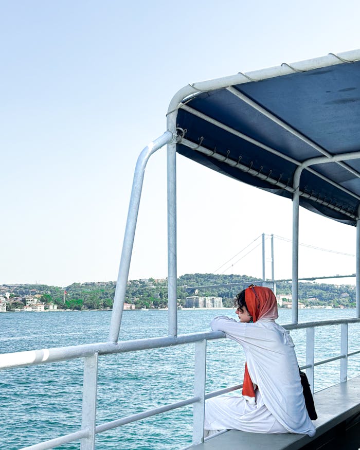 A woman in a red shawl enjoys the scenic Bosphorus view in İstanbul, Türkiye.